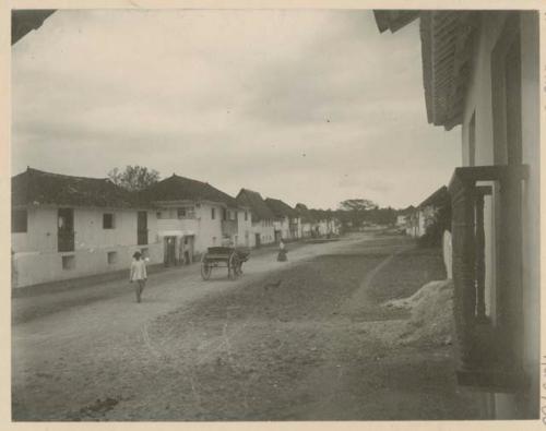 Man, woman and cart in middle of road lined with buildings at Agana