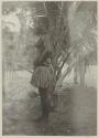 Man standing in front of palm, side view