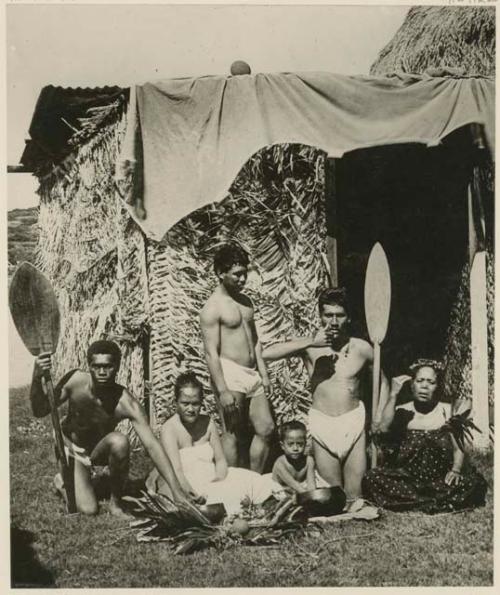 Group of people in front of structure made from woven palm fronds