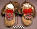 Pair of skin moccasins with red cloth frontice covered with beaded design