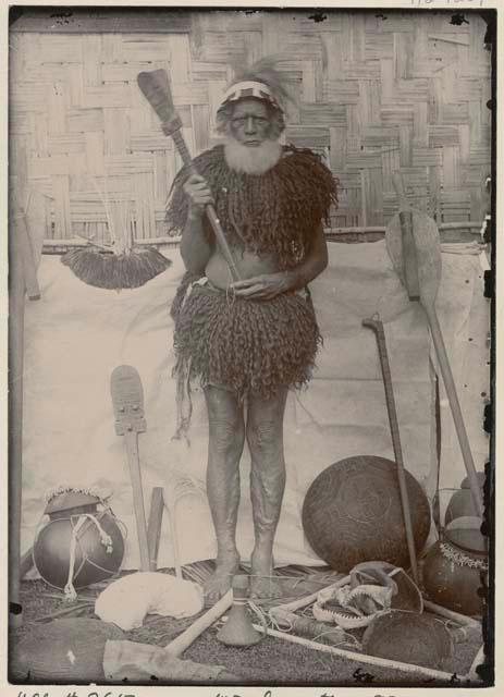 Man with beard and headdress, holding club and surrounded by objects