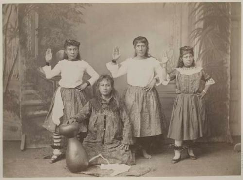 Three women hula dancers, one woman seated with gourd drum