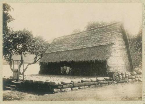 People sitting in front of thatched structure with stone platform