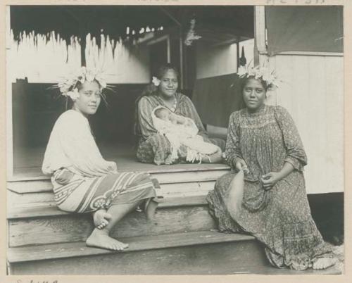 Three women sitting on steps one holding an infant