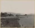 Dugout canoe along a shore with long pier and buildings in the background