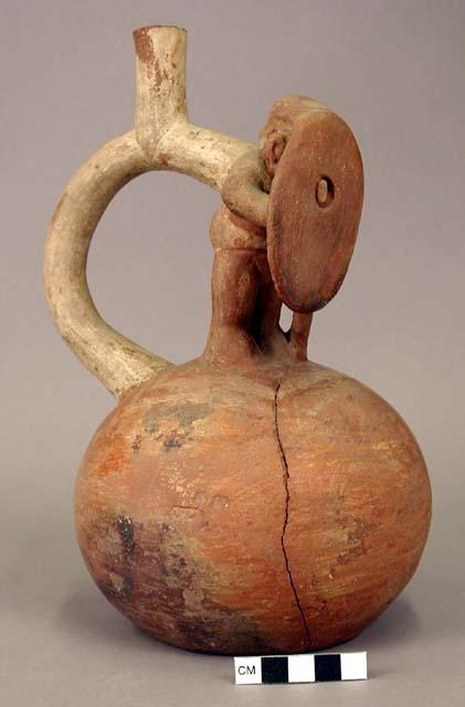 Ceramic bottle, stirrup spout, with molded human effigy figure holding shield an