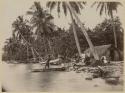 Man in canoe throwing spear, people on shore outside building