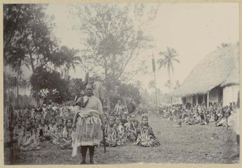 Crowd seated on ground with man standing in front