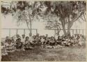 Women seated with arms up, men seated behind them