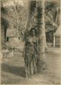 Woman leaning against tree, with houses in background