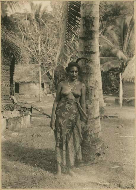 Woman leaning against tree, with houses in background