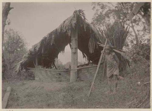 Person in front of a shelter with carved wooden post