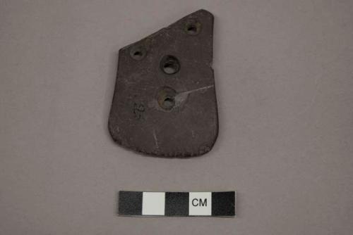 Archaeological, ground stone pendant with four drilled holes, one edge has several small incised lines.