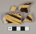 Yellow and brown slip decorated earthenware vessel body and rim fragment, buff paste, crimped rim