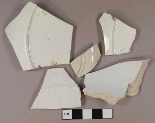 Undecorated white pearlware vessel body, rim, and base fragments, white paste