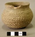 Ceramic vessel, corrugated, short and flared neck, chip in rim, flat base.
