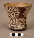 Brown goblet painted in white with nine rayed faces and one rosette