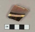 Dark brown and yellow slip decorated earthenware vessel body fragment, buff paste