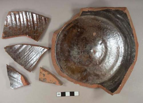 Dark brown lustrous lead glazed interior redware vessel body and base fragments, visible temper