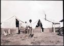 Hopi man standing in front of two tents