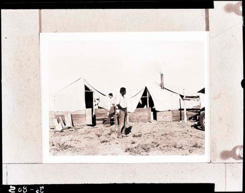 Hopi man standing in front of two tents
