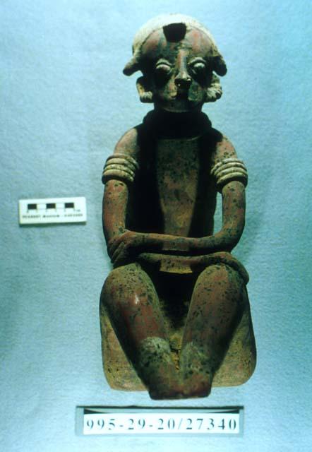 Seated male figure with bony spine and arms crossed over knees