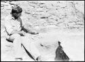 Watson Smith sitting on kiva bench. Wall shows imprint of matting. Test 19, Room 3, E wall.