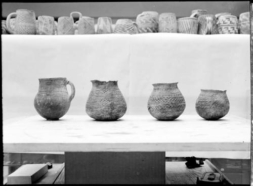 Four large pots, smaller pots & mugs above on shelf.