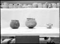 Three large pots, smaller pots & mugs above on shelf.