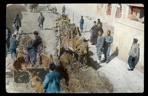 Lantern slide of carts on rutted road, hand-colored