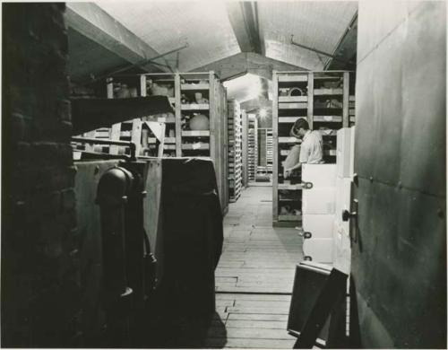 Historical photograph of Peabody Museum attic storage with various objects and a Peabody employee