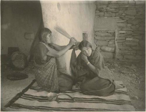 Two Hopi women, one giving the other the squash-blossom hairstyle