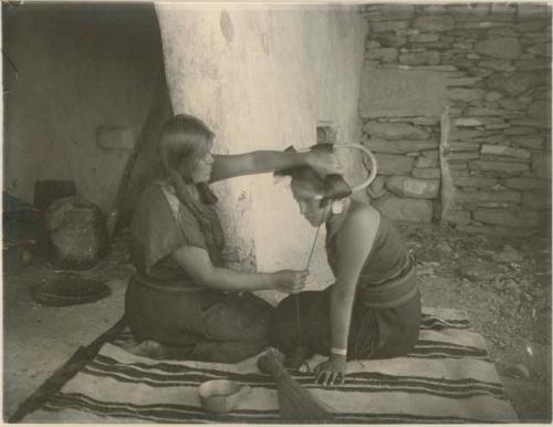 Two Hopi women, one giving the other the squash-blossom hairstyle