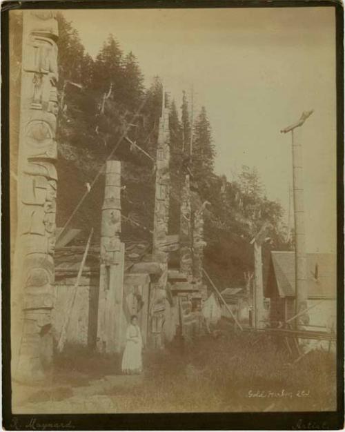 Totem poles at New Gold Harbor, British Columbia, woman in foreground.