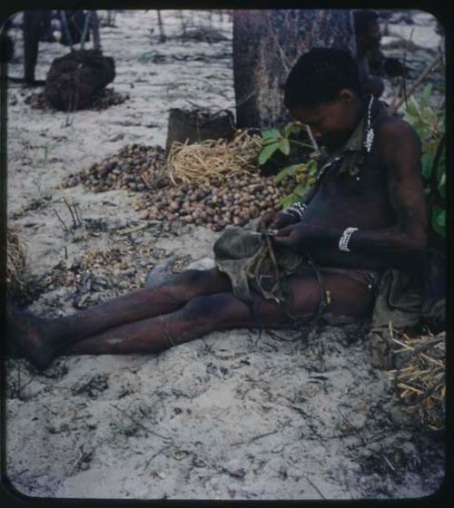 Food Gathering, "Manghettis": Boy mending a bag, sitting by a mangetti tree and a pile of nuts