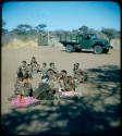 Expedition: Group of women sitting, with blankets on the ground next to them, an expedition truck in the background