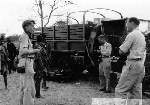 People standing with John Marshall and other expedition members next to the trucks