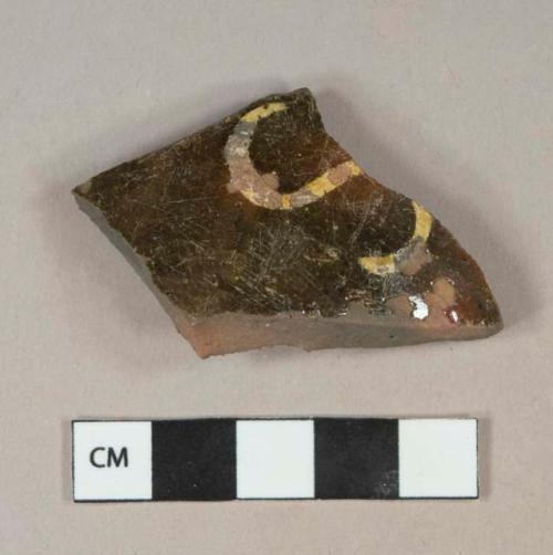 Yellow on dark reddish brown slip decorated redware vessel body fragment