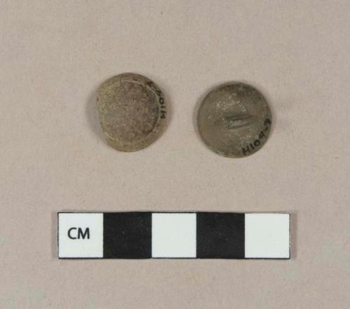 Two halves of a metal button - domed top and bottom. Top has possible molding, bottom has loop shank and possible silver plating