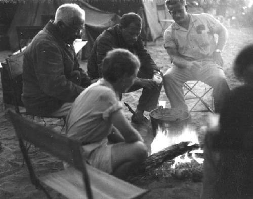 Elizabeth Marshall Thomas and Laurence Marshall sitting next to a fire with other expedition members