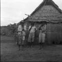 Portraits of people: three men outside thatched building