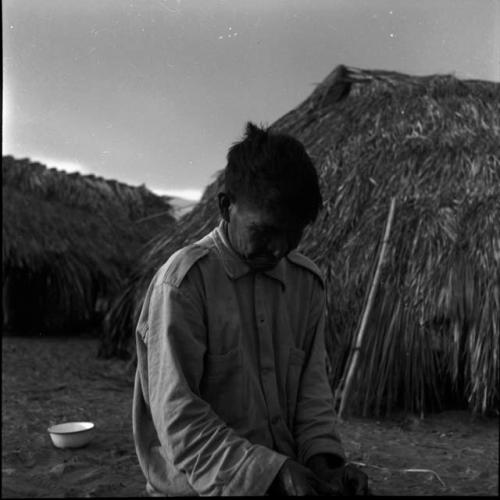 Portraits of people: man sitting outside thatched building