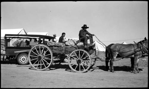 Two Hopi riding with Everett Harris on his wagon, Dodge truck behind