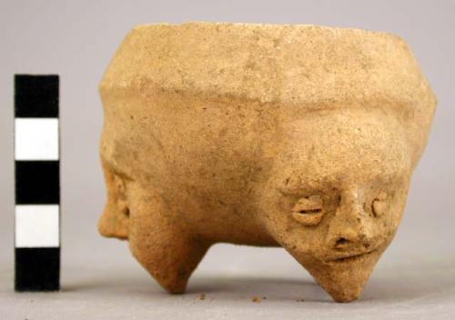 Unpainted tripod vessel with a human effigy face on each leg.