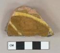 Yellow on brown slip decorated redware vessel base fragment, burned exterior