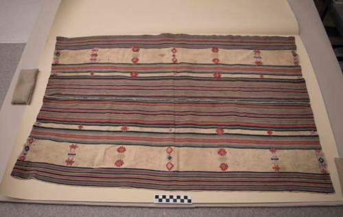 Woven white textile, flat, with multicolored bands and embroidered designs