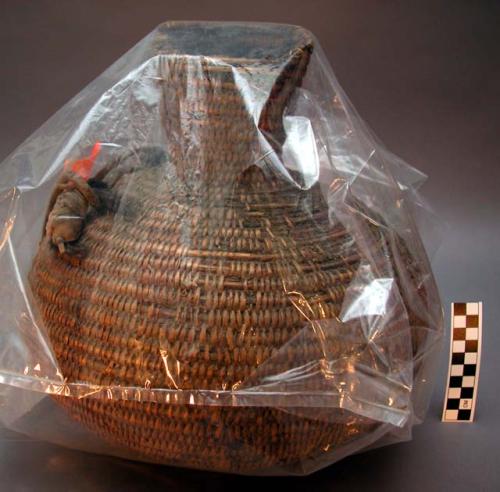 Water jug, basket work. Made of bear grass, covered with pitch. Leather strap.