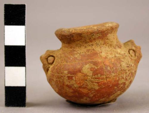 Miniature red incised globular vessel with stylized animal head handles.