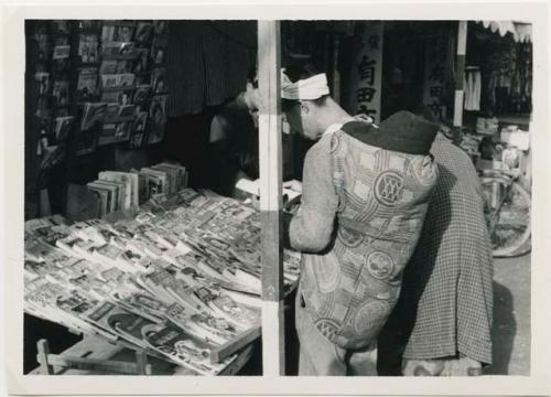 Man carrying baby on his back in winter cover, at bookstall