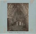 Man drawing or sketching inside a stone room with artifacts and tools on the walls